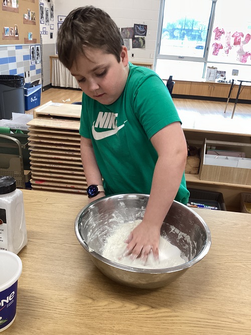 A child using their hand to mix playdough in a bowl.