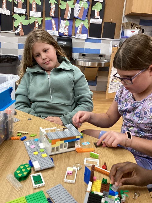 Two children sitting at a table building with lego.
