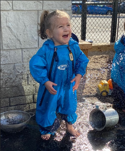 A child smiling while exploring with mud.