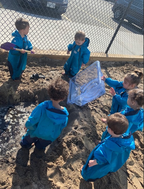 A group of children exploring with a sensory bin in the sandbox.