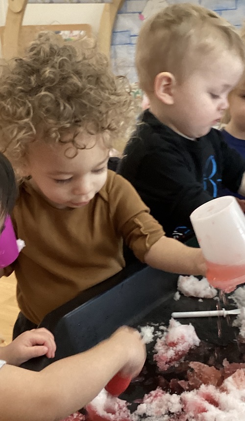 Children exploring with cups, droppers, paint brushes and coloured snow.