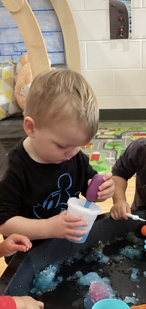 A child using a dropper with coloured snow in a cup.
