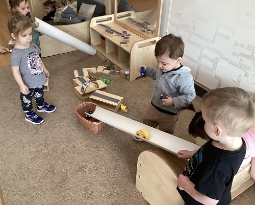 A small group of children taking turns to drive their cars down the ramp they created.