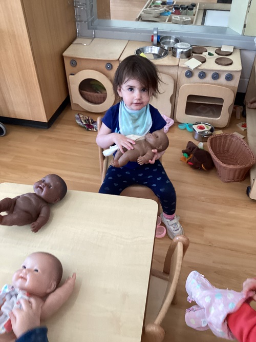 A child engaging in dramatic play as they are sitting and caring for a baby.