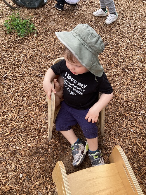 A child sitting with their baby in a chair on the playground.