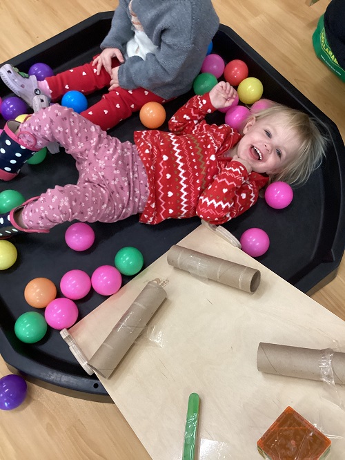 A toddler excitedly laying in the tuff tray surrounded by balls