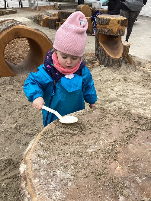 A child patting sand down on a stump table in the sandbox.