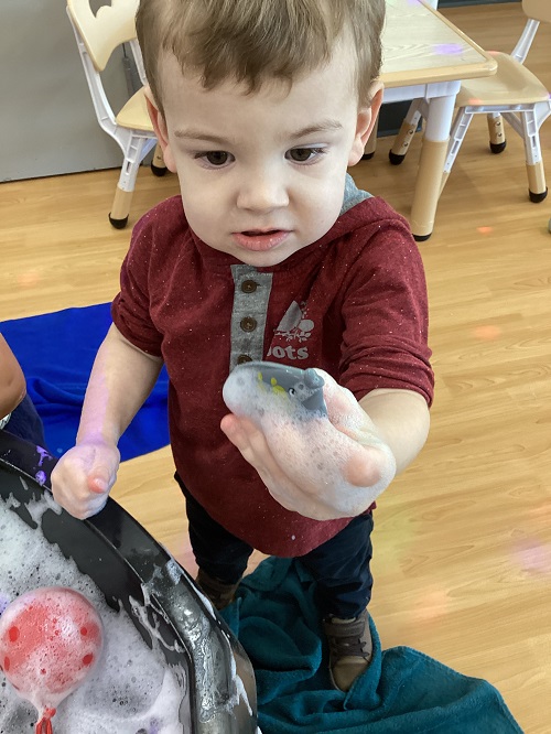 A child holding an item they found in the tuff tray.