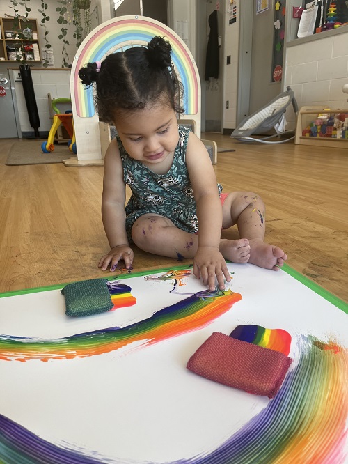 An infant child creating a rainbow art piece