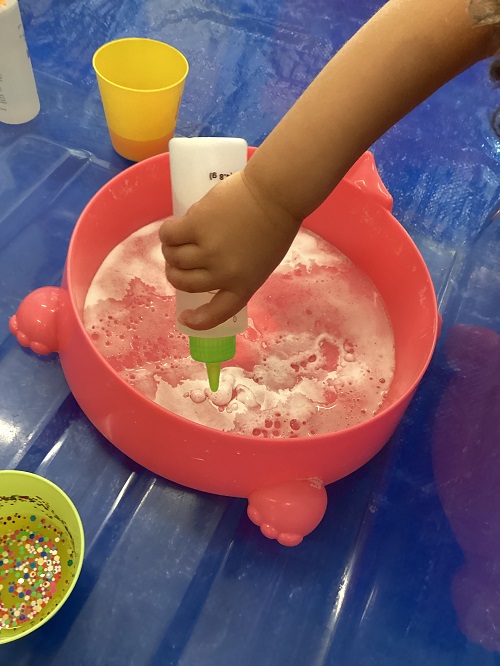A child squeezing paint into shaving foam