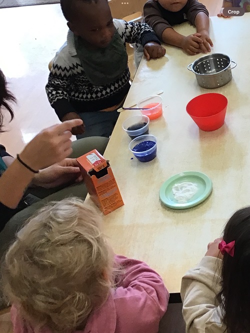 5 Toddler children sitting around the table looking at the cups with coloured paint, bowls, baking soda and strainer on the table