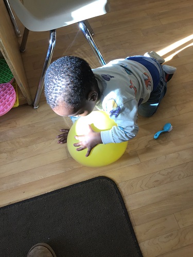 Toddler chgild kneeling on the ground and leaning is one arm on top of a balloon