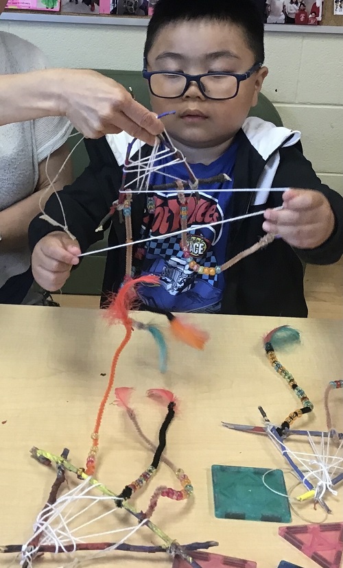 One child sitting at a table using string to create a dream catcher