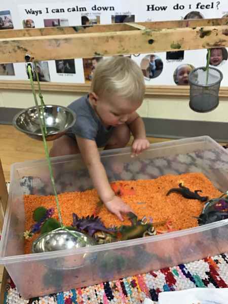 toddler playing in a filled sensory bin