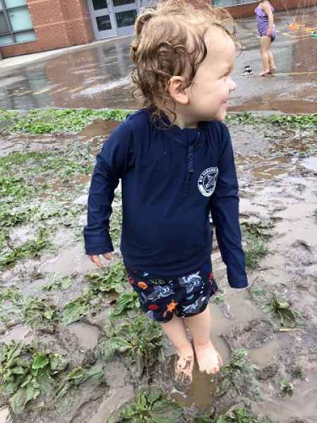 boy smilig standing in a mud puddle in his bathing suite