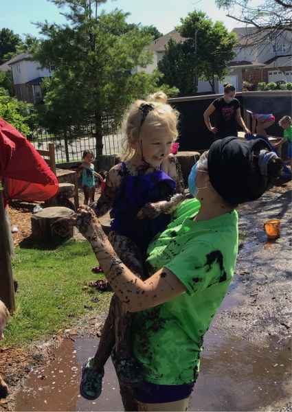 educator holding a happy child and they are both covered in mud on mud day