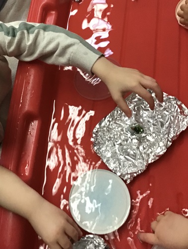 Preschoolers are placing their homemade boats into water to see if they float.