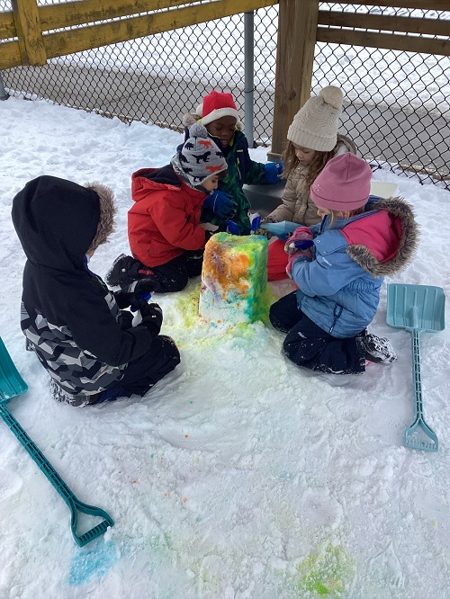 Children kneeling down around a colourfulsnow tower