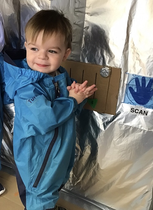 child in pretend space suit in a space ship made from a cardboard box