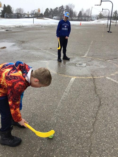 two children playing ball hockey outside