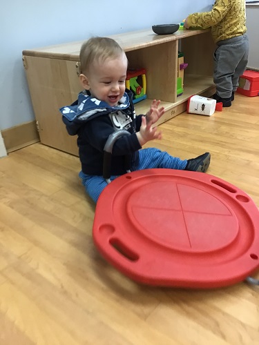 infant sitting beside a spin toy