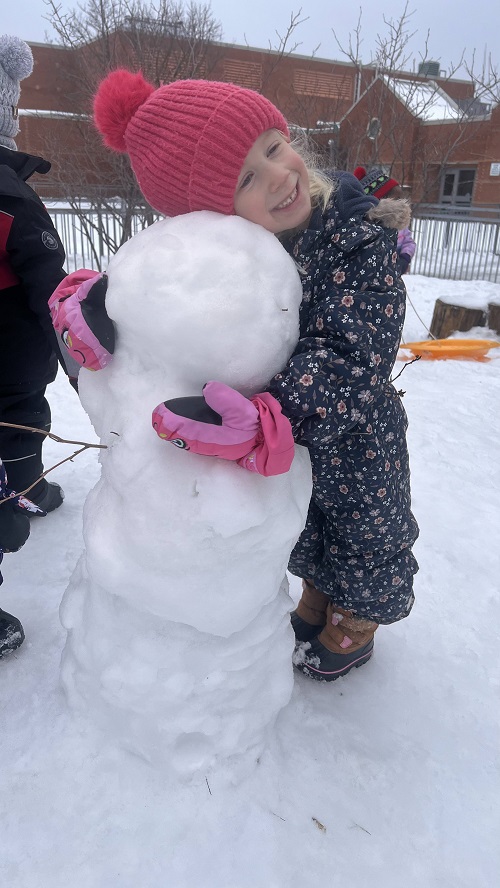 child hugging their homemade snowman