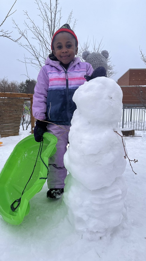 child standing beside a snowman on the playground