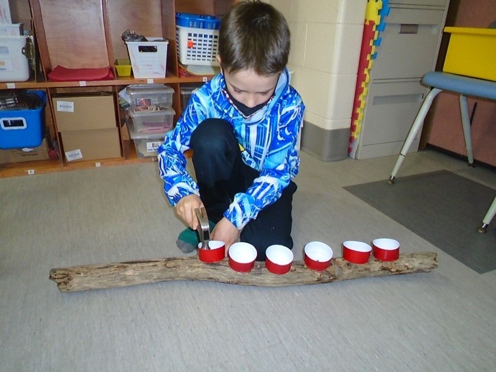 Child hammering plastic cups to a wooden log