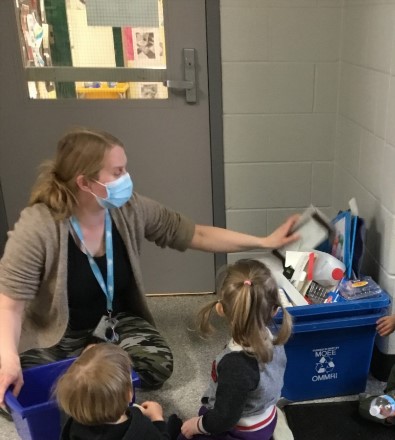 Educator and children kneeling by a recycle bin