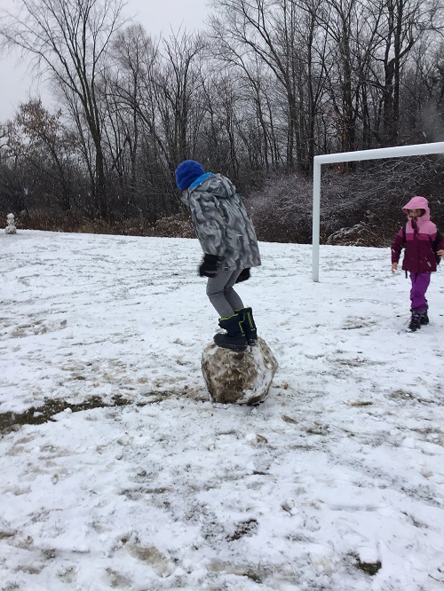 Child standing on a large snowball.