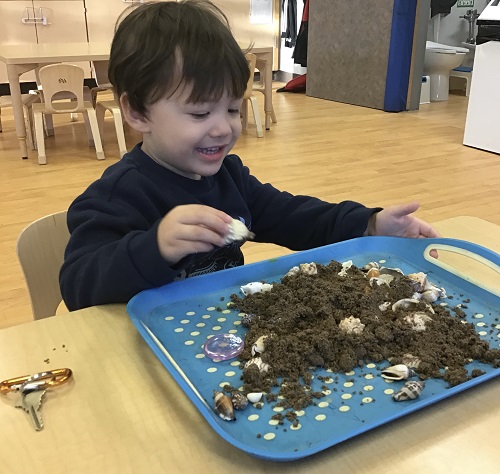 Preschool child manipulating sand and loose parts