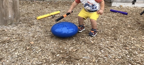 Toddler child creating sound with the stick on the drum