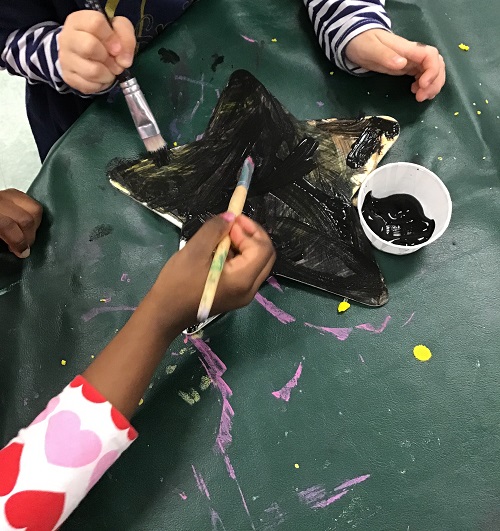 Children painting a wooder star shape together.