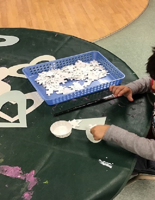 Child gluing painted puzzle pieces on paper.