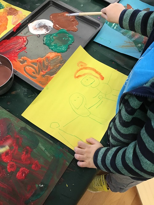 Child painting a picture of what comes to mind when they think of yellow, on yellow paper.