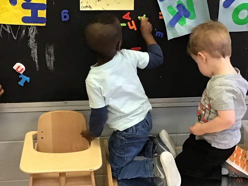 Child placing magnetic letters on a blackboard.