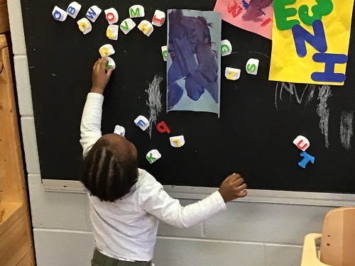 Child reaching for a magnetic letter on the blackboard. 