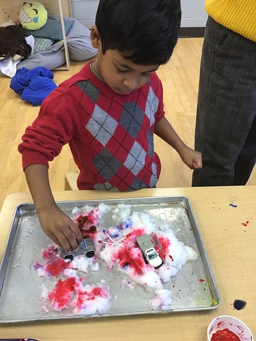 Child driving car through snow on a tray, in the classroom.