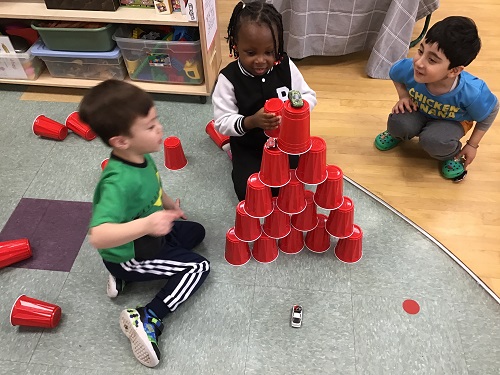 Group of children building tower with car on top, out of solo cups.