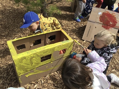 Children painting a box with yellow paint outside.