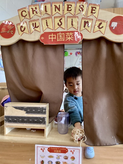 A preschool child engaged in imaginative play at a Chinese cuisine restaurant