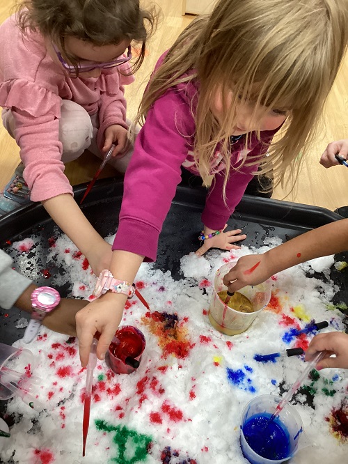 Children using water droppers to add colour to fresh white snow.
