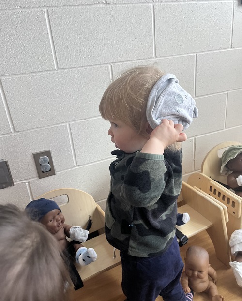 An infant trying to put a hat on their head