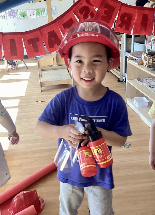 A preschool child dressed up like a firefighter holding a toy fire extinguisher