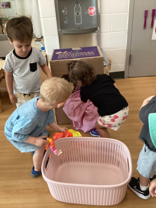 Toddler children putting clothes in a cardboard laundry machine