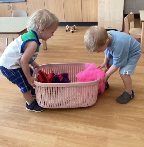 Toddler children putting clothes in a laundry basket