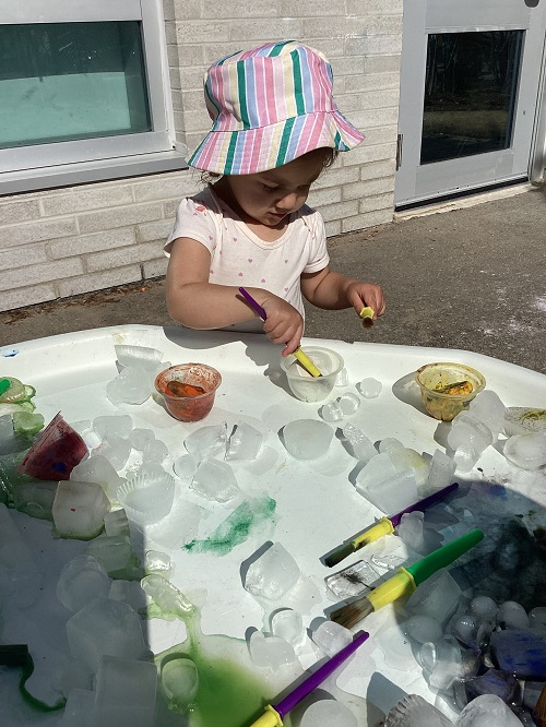 A toddler painting ice cubes on the tuff tray