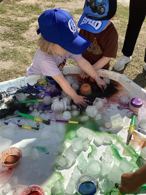 A group of toddlers painting ice on the tuff tray