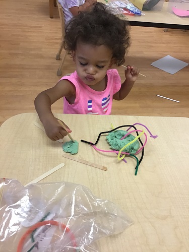 toddler girl using pipe cleaners and play dough 