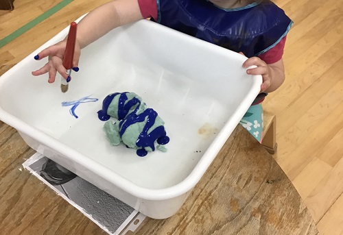white bucket filled with soapy water, toddler hand reaching in to wash toy